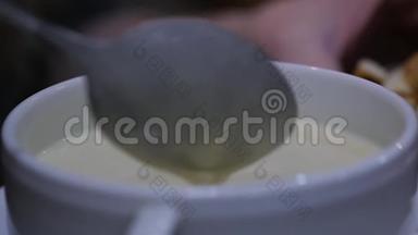 在一个碗里加奶酪汤，女孩用勺子搅拌汤。 慢动作